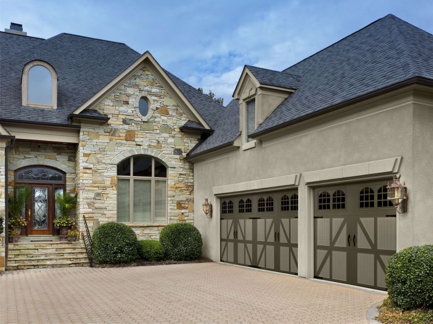 A home with a brown-brick exterior has a three-car garage. The doors are light and dark brown with arched windows.