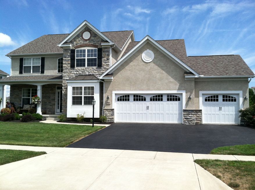 A two-story home with a three-car garage. The garage is white with vertical panels and a top row of arched windows.