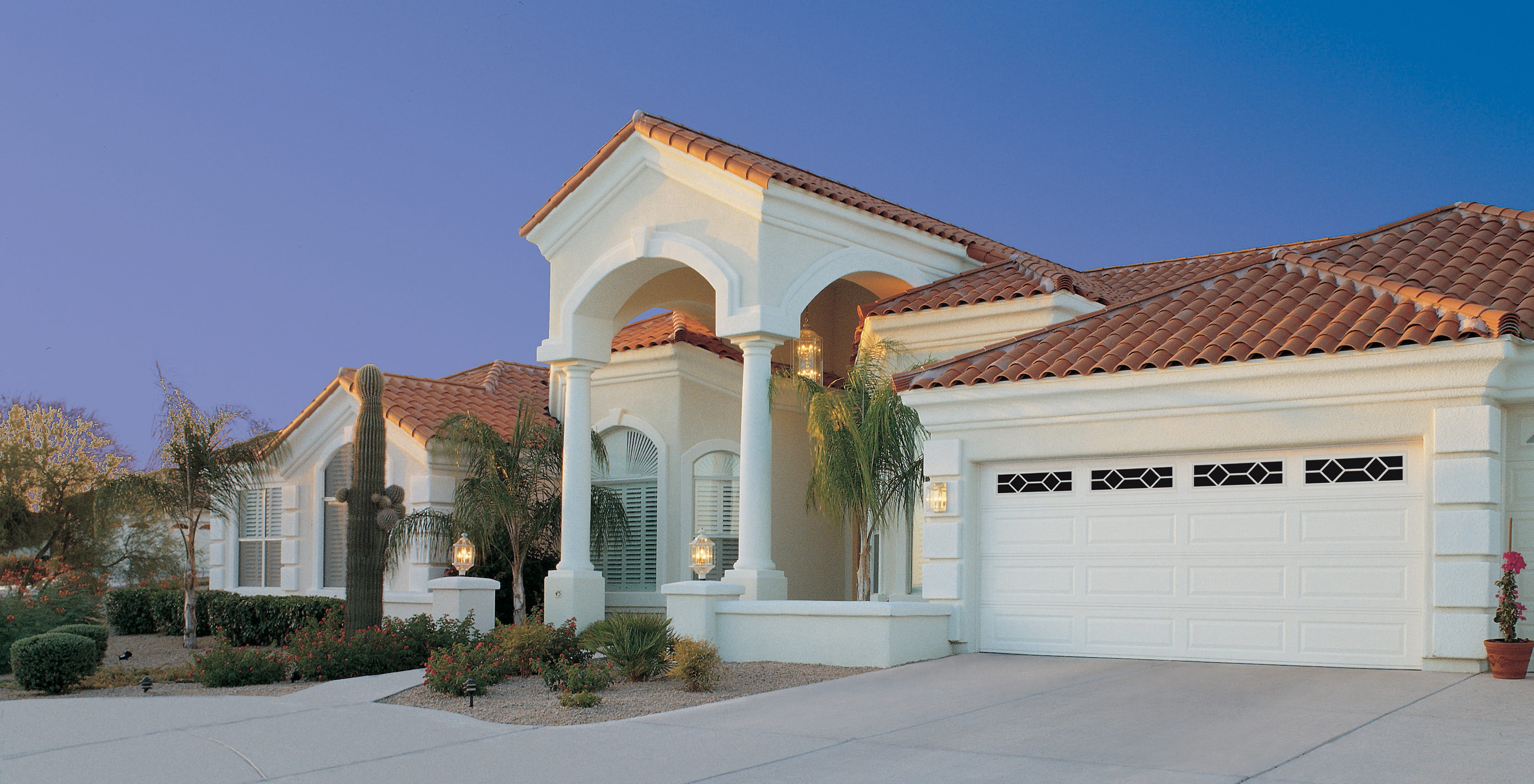 A home with a white exterior and a rust-colored roof has a garage with detailed windows. The entryway has large columns.